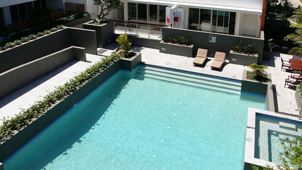 Una piscina rectangular con borde alicatado, rodeada de muros bajos y plantas en macetas.