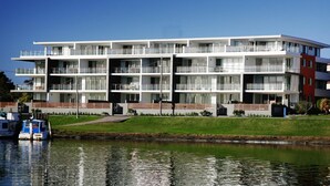 Un edificio moderno de varios pisos con balcones, situado junto a una masa de agua tranquila.