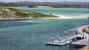 A pier extending into a turquoise body of water with a clear sky above. - Wharf Street Vista (Forster)