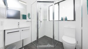 A modern bathroom with a glass-enclosed shower, white fixtures, and a large mirror. - Wharf Street Vista (Forster)