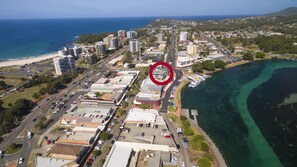 An aerial view of a coastal city with a mix of commercial and residential buildings, a marina, and a beach. - Wharf Street Vista (Forster)