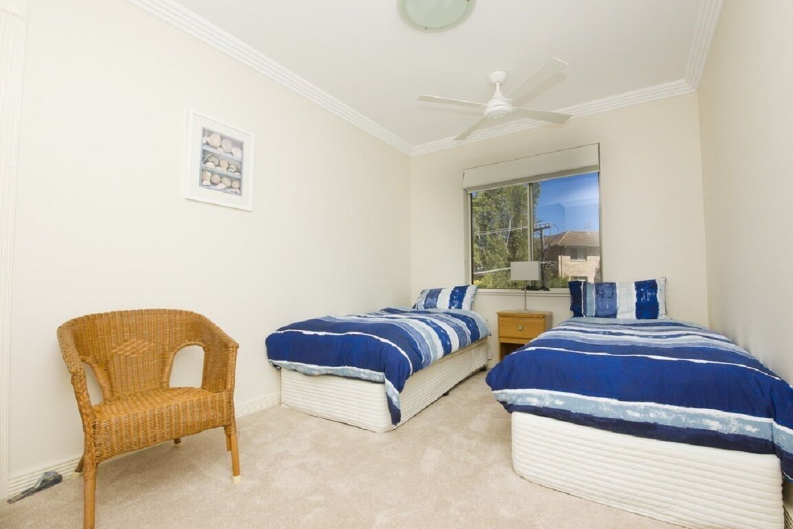 A bedroom with two beds, a chair, a ceiling fan, a window, and a framed picture on the wall.