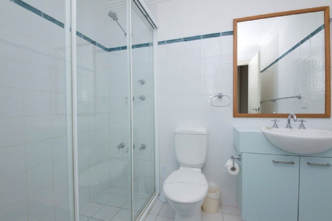 Ein Badezimmer mit einer Duschkabine, einer weißen Toilette, einem Waschbecken mit Spiegel und einem Schrank mit Handtuchhalter.