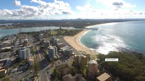 An aerial view of a coastal city with a beach, buildings, and a bridge. - Whitesands Unit 103 (Forster)