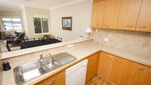 A modern kitchen with wooden cabinets, a stainless steel sink, and a dishwasher. - Whitesands Unit 103 (Forster)