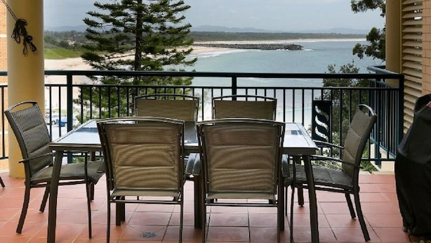 Een balkon met een tafel en stoelen, met uitzicht op een strand en de oceaan.
