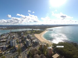 An aerial view of a coastal city with a beach, buildings, and a bridge. - Whitesands Unit 402 (Forster)