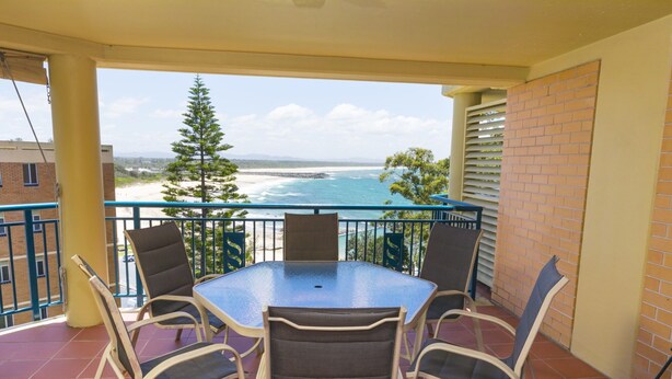A balcony with a table and chairs, overlooking a beach and ocean. - Whitesands Unit 602 (Forster)