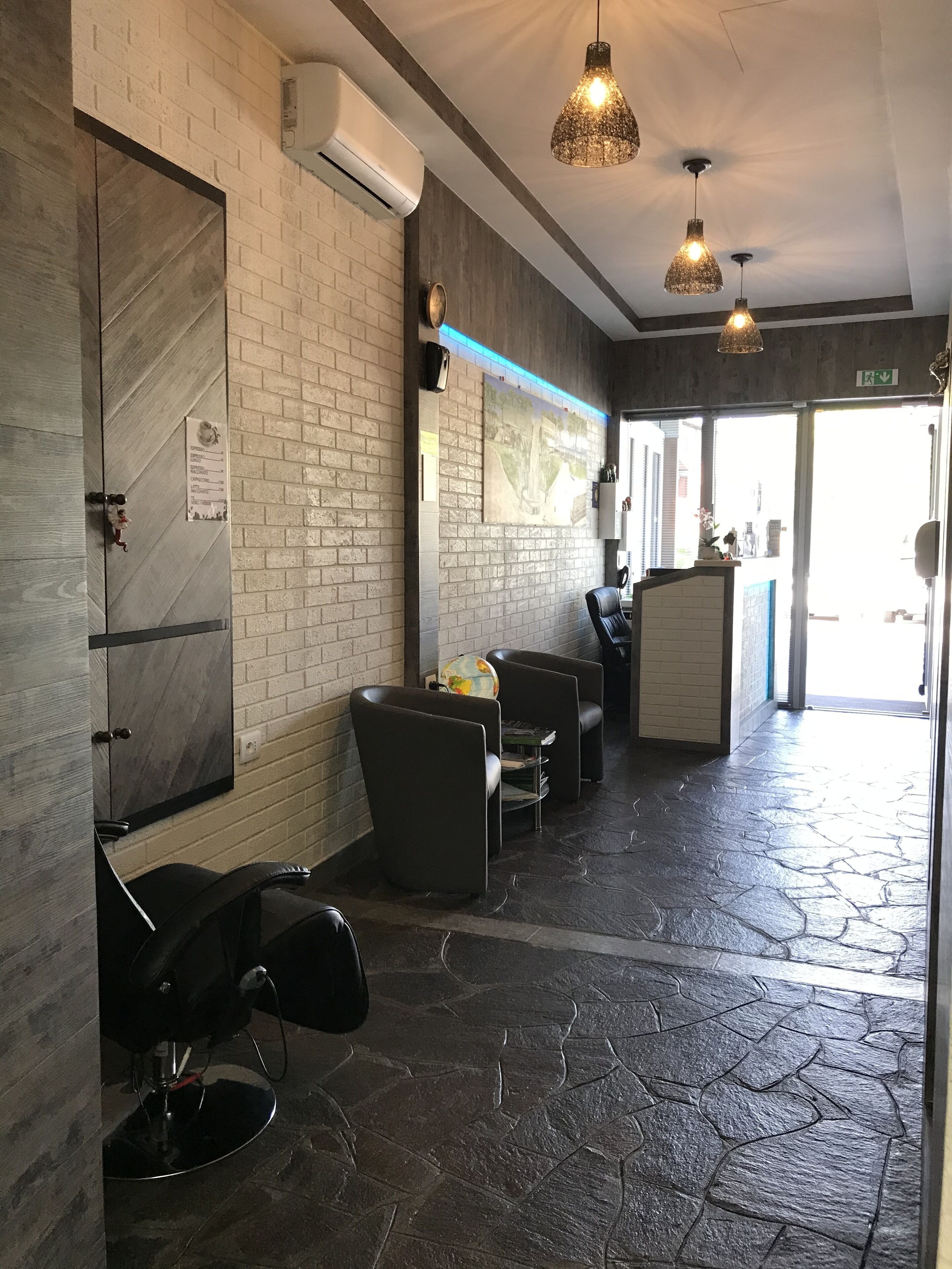 A hair salon interior with brick walls, black leather chairs, and a stone-patterned floor.
