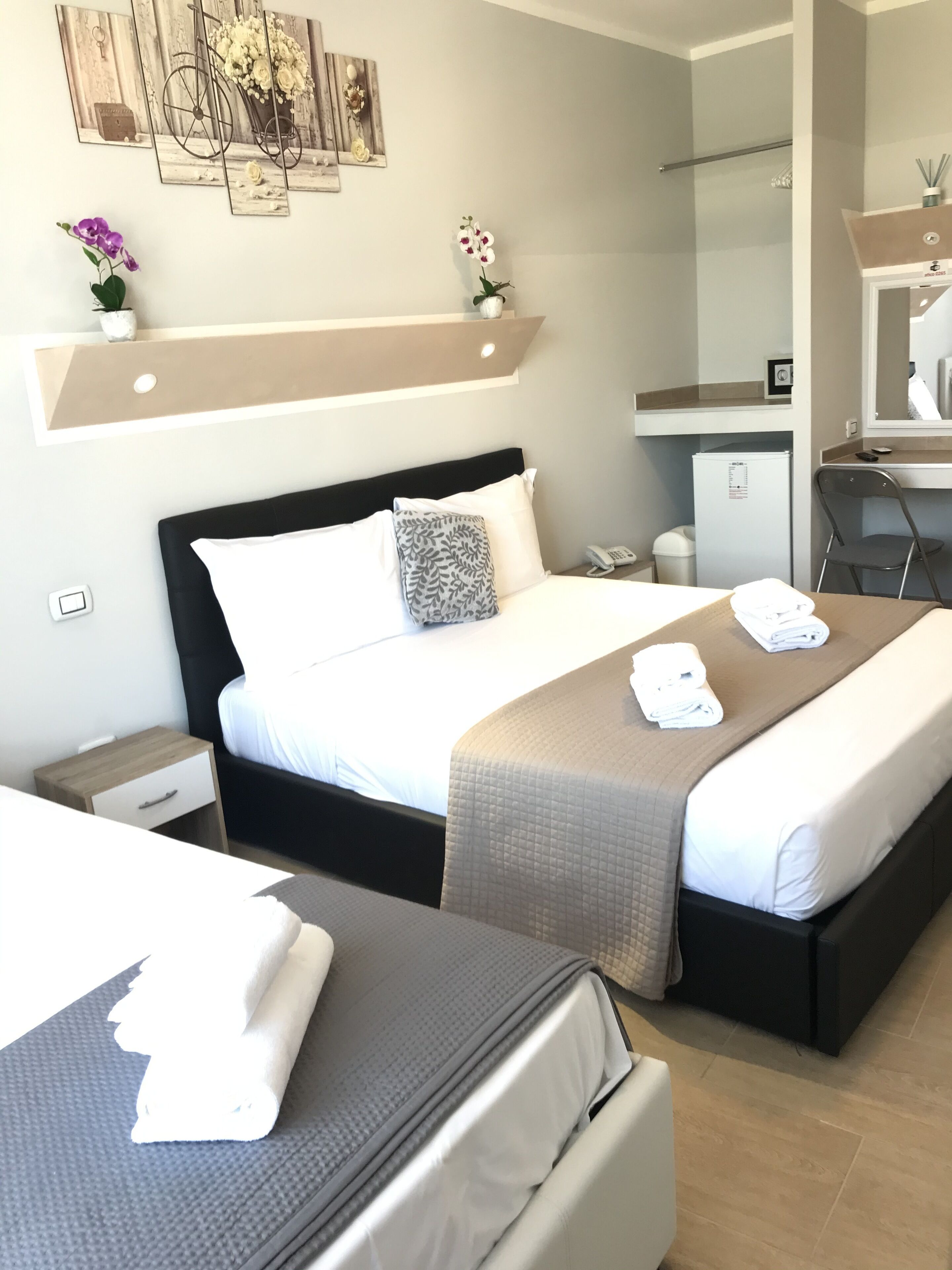 A hotel room with a large bed, a smaller bed, a desk, a chair, a mirror, and a refrigerator.