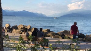 A lakeside walkway with benches, a sailboat on the water, and mountains in the background. - Atico Hotel (Desenzano del Garda)