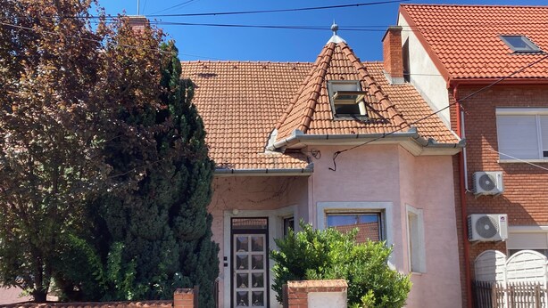 A two-story house with a tiled roof, a front door with a small window, and a brick wall. - Peregrino Vendégház (Budaors)