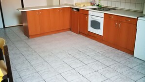 A kitchen with wooden cabinets, a white stove, and a tiled floor. - Peregrino Vendégház (Budaors)