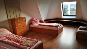 A bedroom with two beds, a wooden dresser, and a window with a city view. - Peregrino Vendégház (Budaors)
