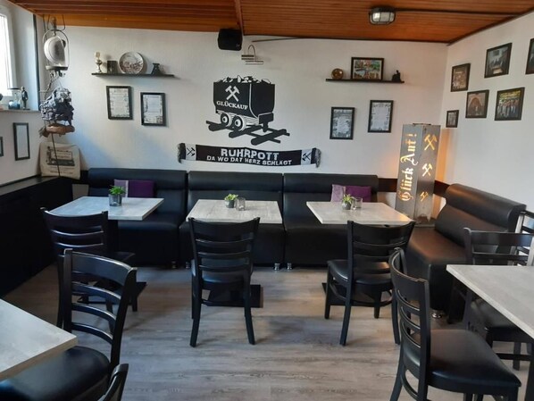 Interior de un restaurante con cabinas, mesas y sillas. Decoración en las paredes y una lámpara en el techo.