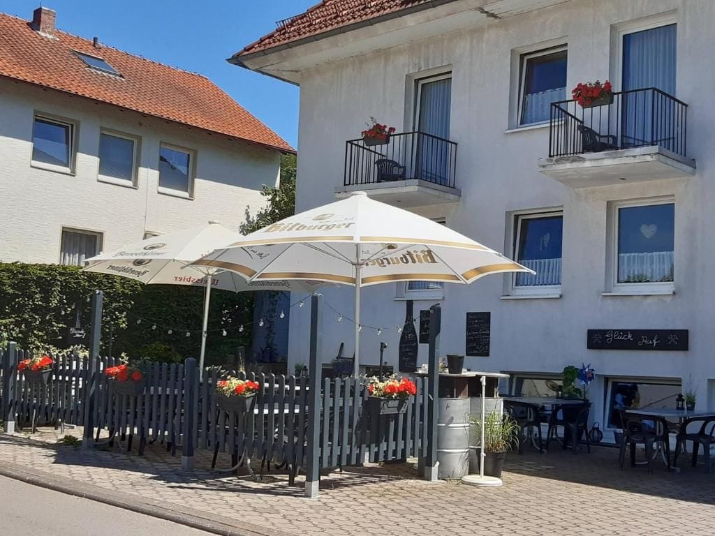 Un edificio con mesas al aire libre y sombrillas, una valla adornada con macetas de flores y un letrero que dice 'Glück Haus'.