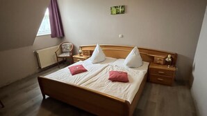 A bedroom with a wooden bed, two bedside tables, a chair, and a window with curtains. - Hotel Vogt (Bad Driburg)