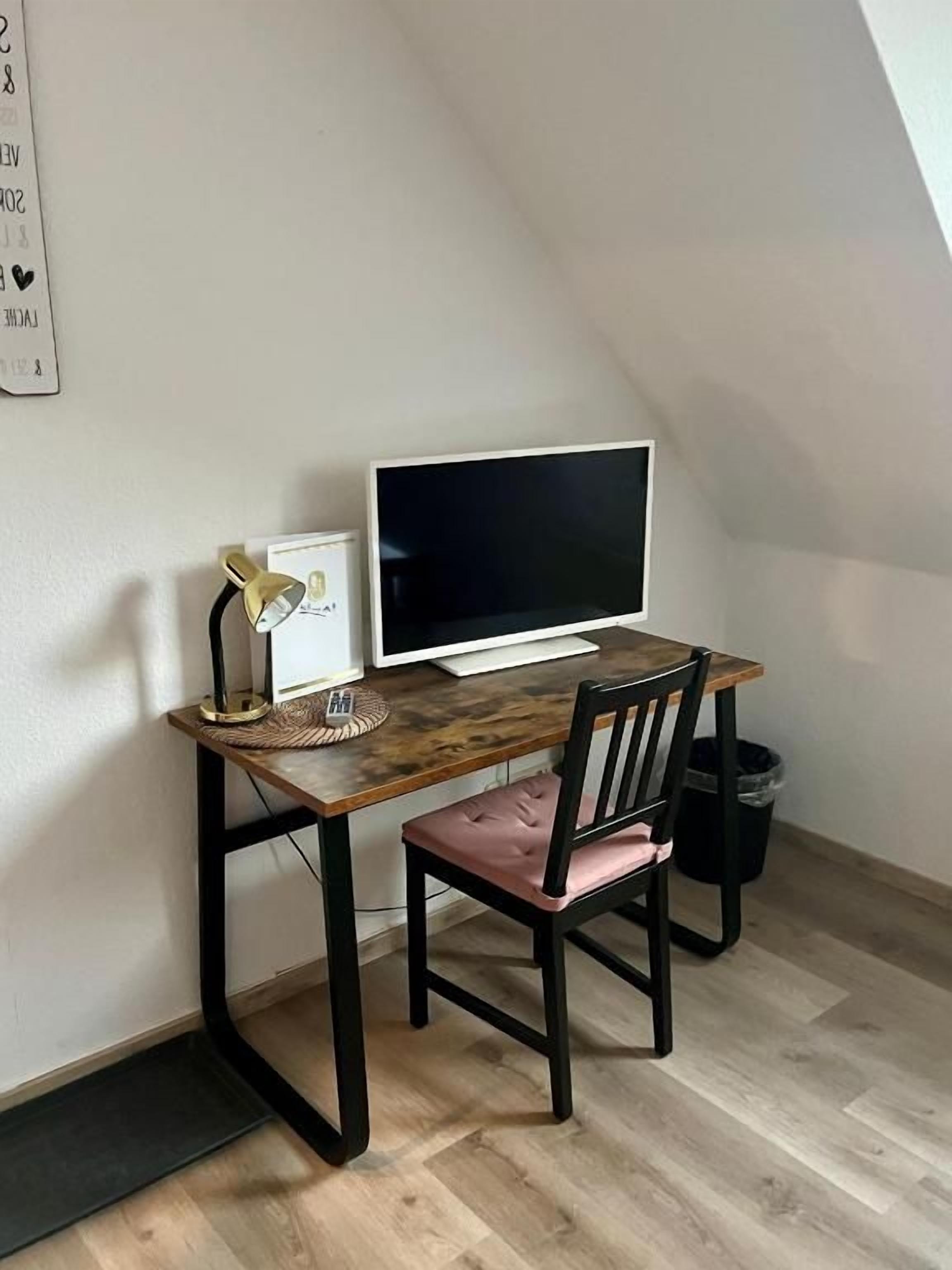 A room with a desk, a computer, a chair, a wall-mounted picture, and a trash can.