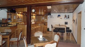 A bar area with wooden furniture, a clock, and a dining area with a table and chairs. - Hotel Vogt (Bad Driburg)
