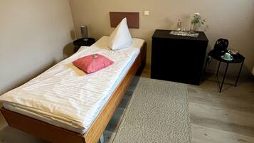 A bedroom with a bed, a bedside table, a nightstand, a small table with a vase, and a wall with text.