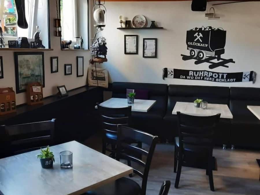 Interior de restaurante com mesas, cadeiras e uma parede decorada com um caminhão e texto.