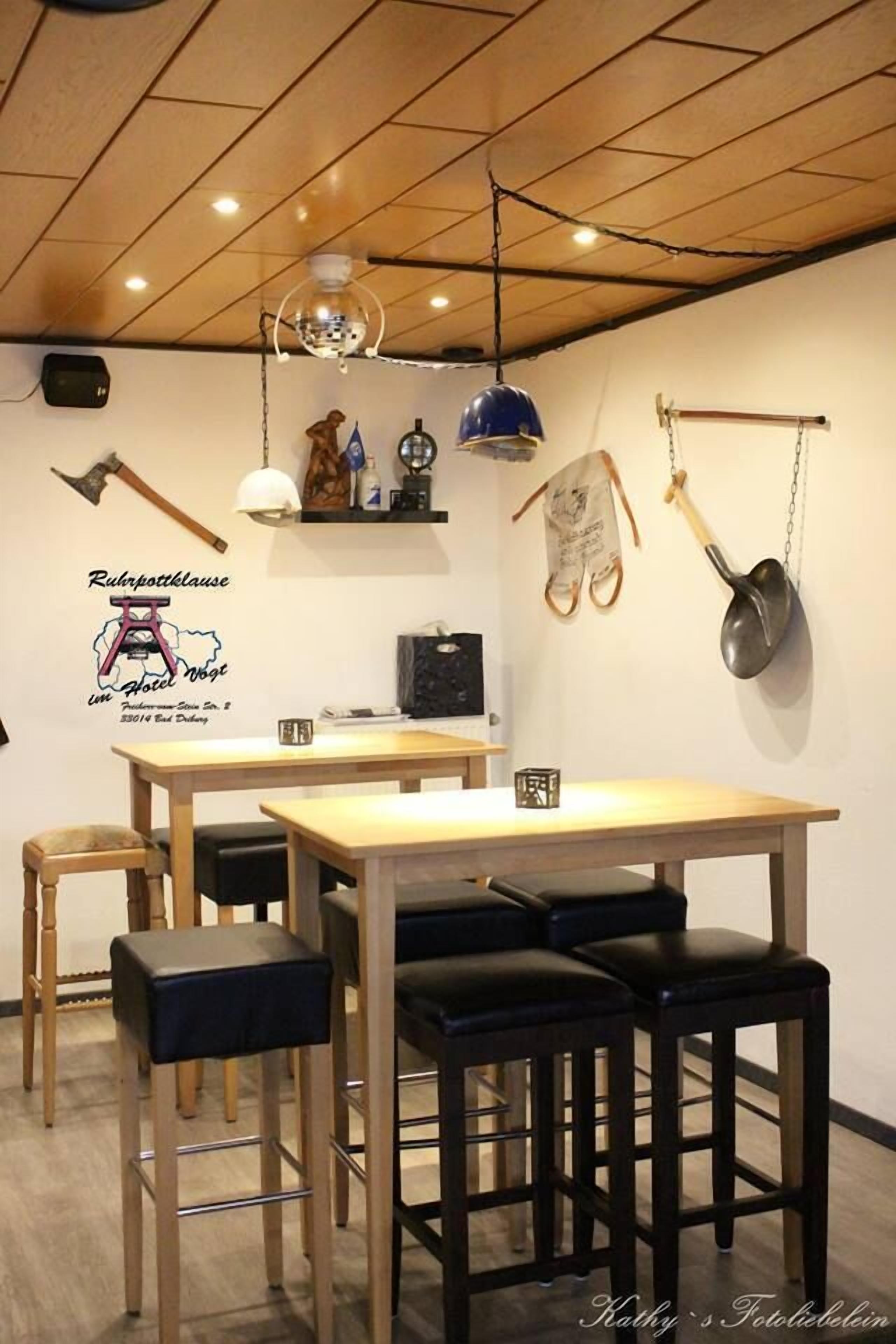 Ein Essbereich mit einem Holztisch, vier Barhocker, einer Hängeleuchte und einer Wand mit einem Logo und einigen dekorativen Gegenständen.