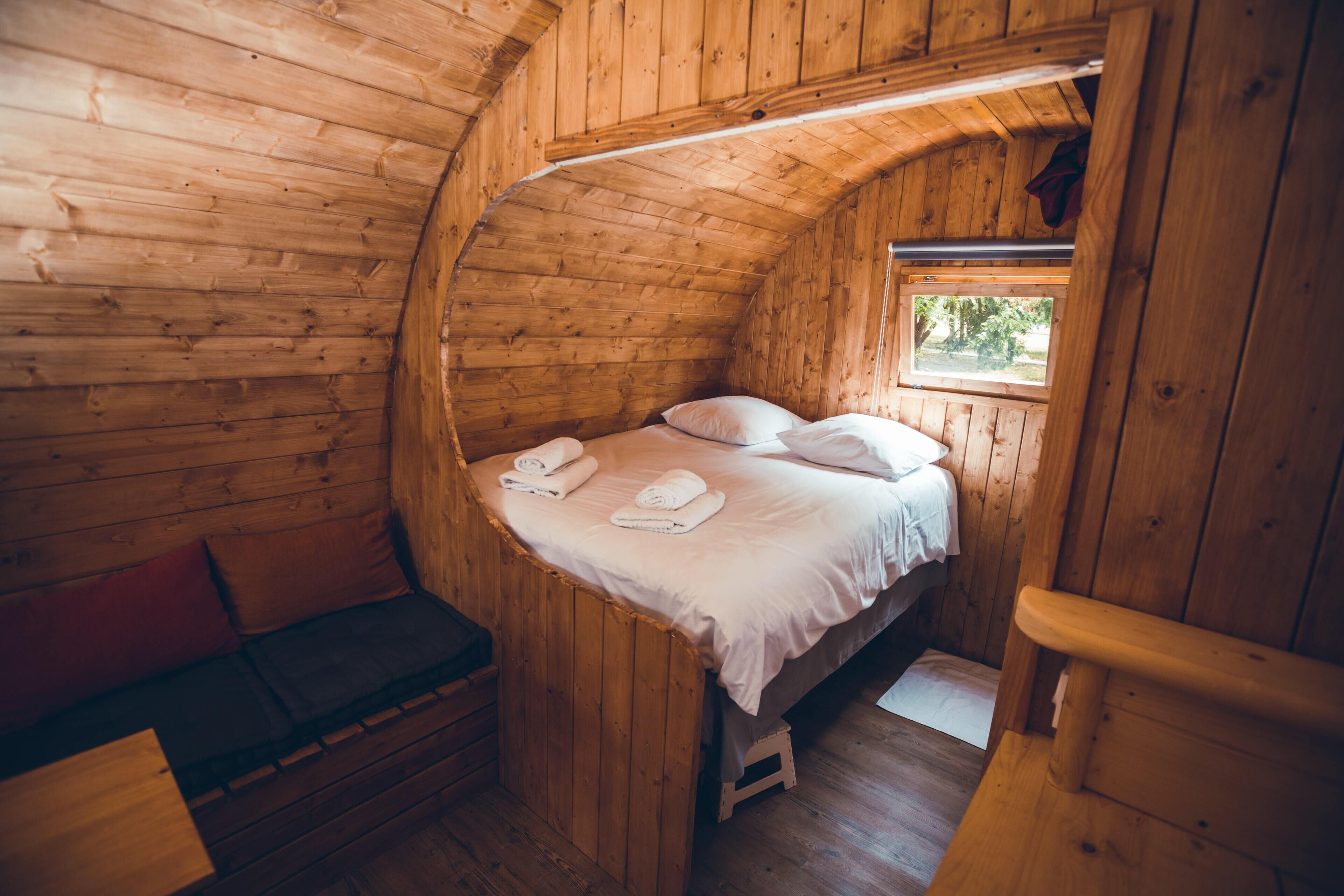 Acogedora habitación de cabaña de madera con una cama, un banco y un ventanal pequeño.