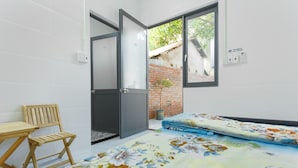 A room with a bed, a wooden chair, a small table, a window, and a brick wall. - King Homestay (Hue)