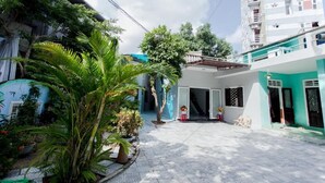 A courtyard with a building featuring a covered entrance, a staircase, and a small seating area. - King Homestay (Hue)