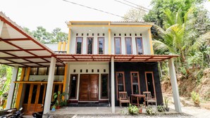A two-story house with a covered porch, a wooden door, and a small outdoor seating area with chairs and a table. - Nabhan Homestay (Kalirejo)