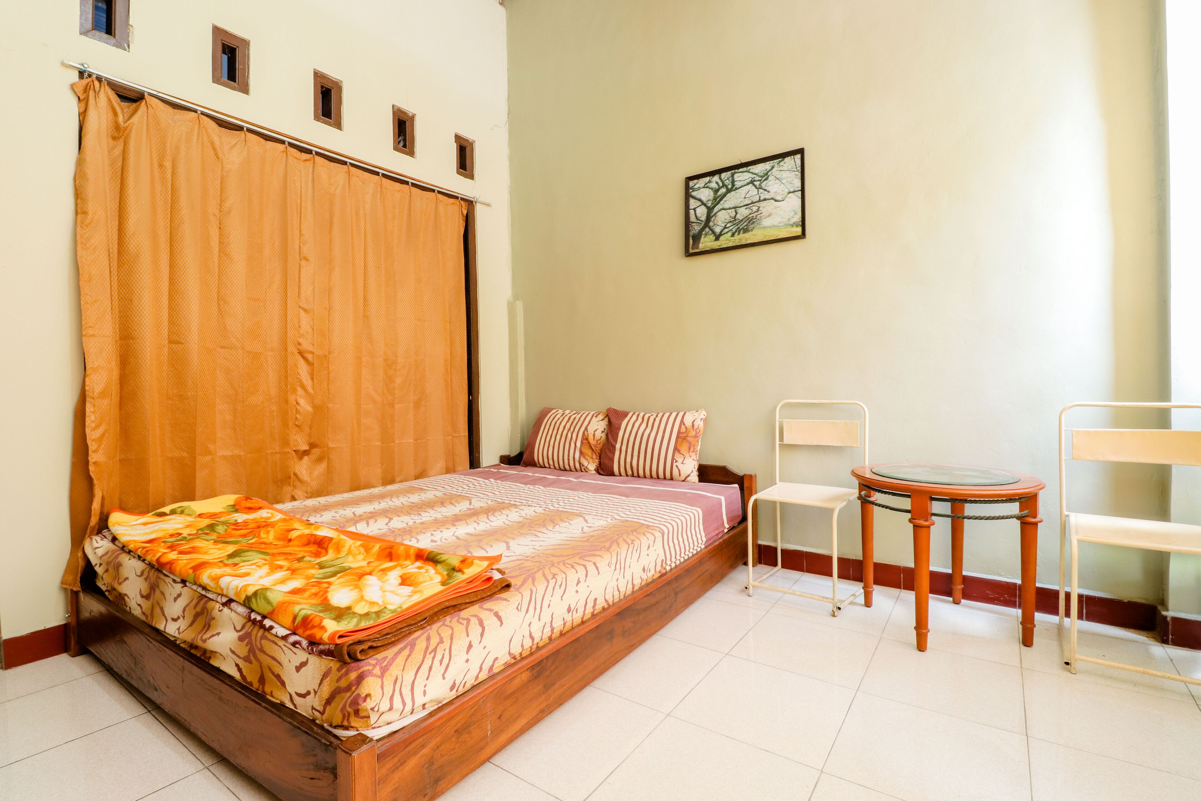 Une chambre à coucher avec un lit, une chaise, une petite table et un tableau accroché au mur.