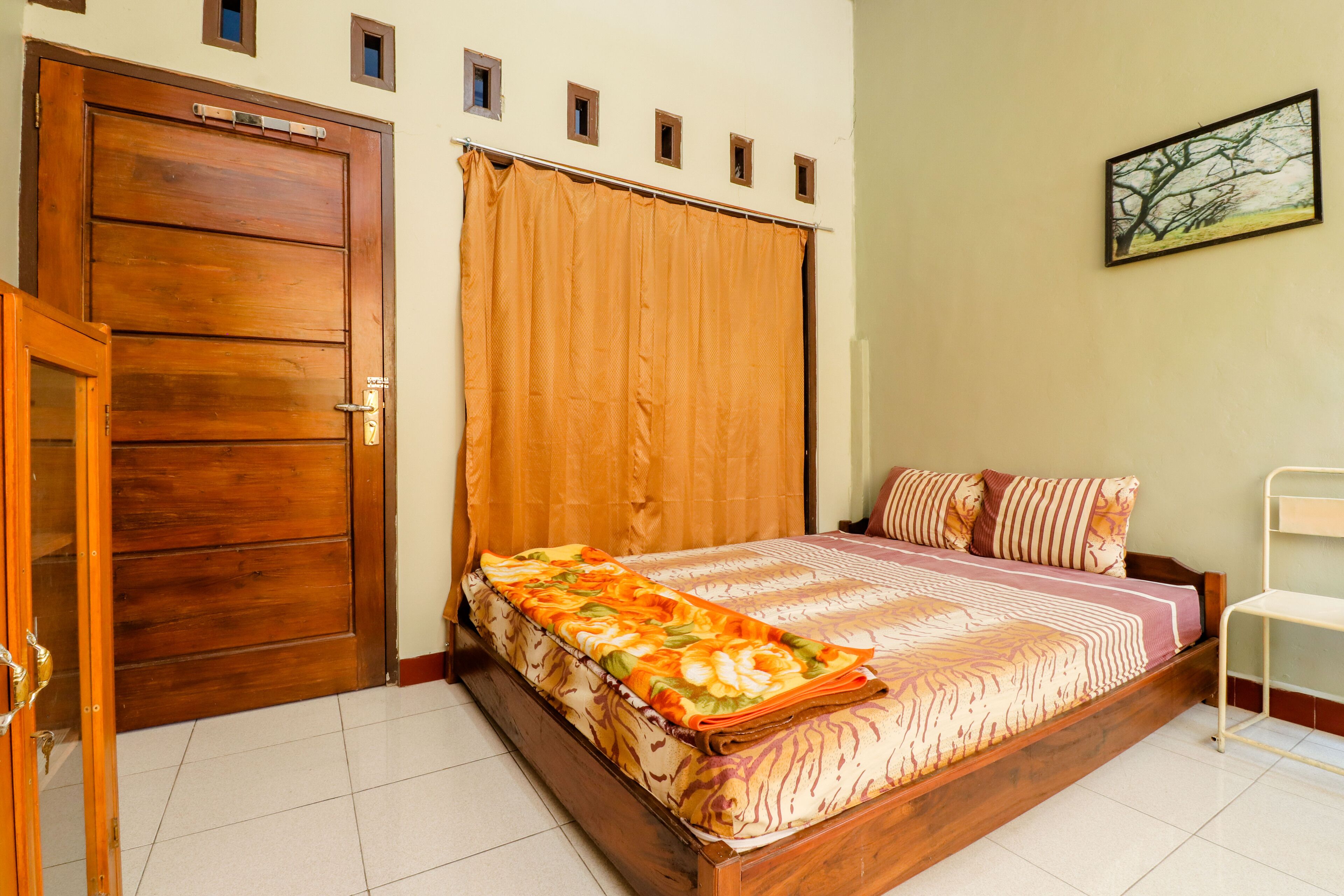 A bedroom with a wooden bed, a large window with curtains, a door, and a painting on the wall.