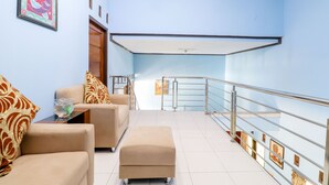 A hotel lobby with a blue wall, a wooden door, a sofa, an ottoman, and a railing. - Nabhan Homestay (Kalirejo)