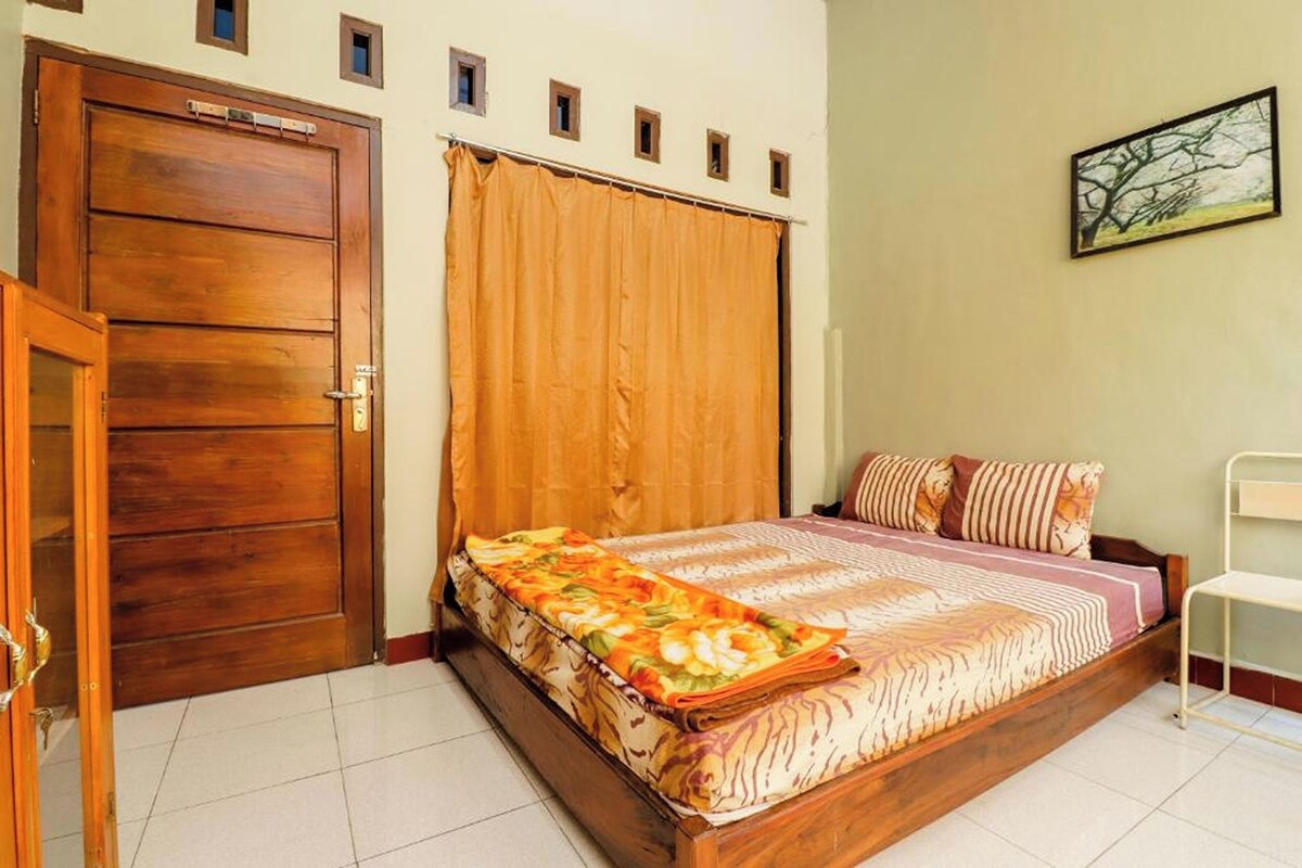 A bedroom with a wooden door, a bed with a floral bedspread, and a painting on the wall.
