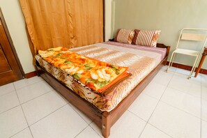 A neatly made bed with a floral bedspread, a wooden headboard, and a metal chair beside it.