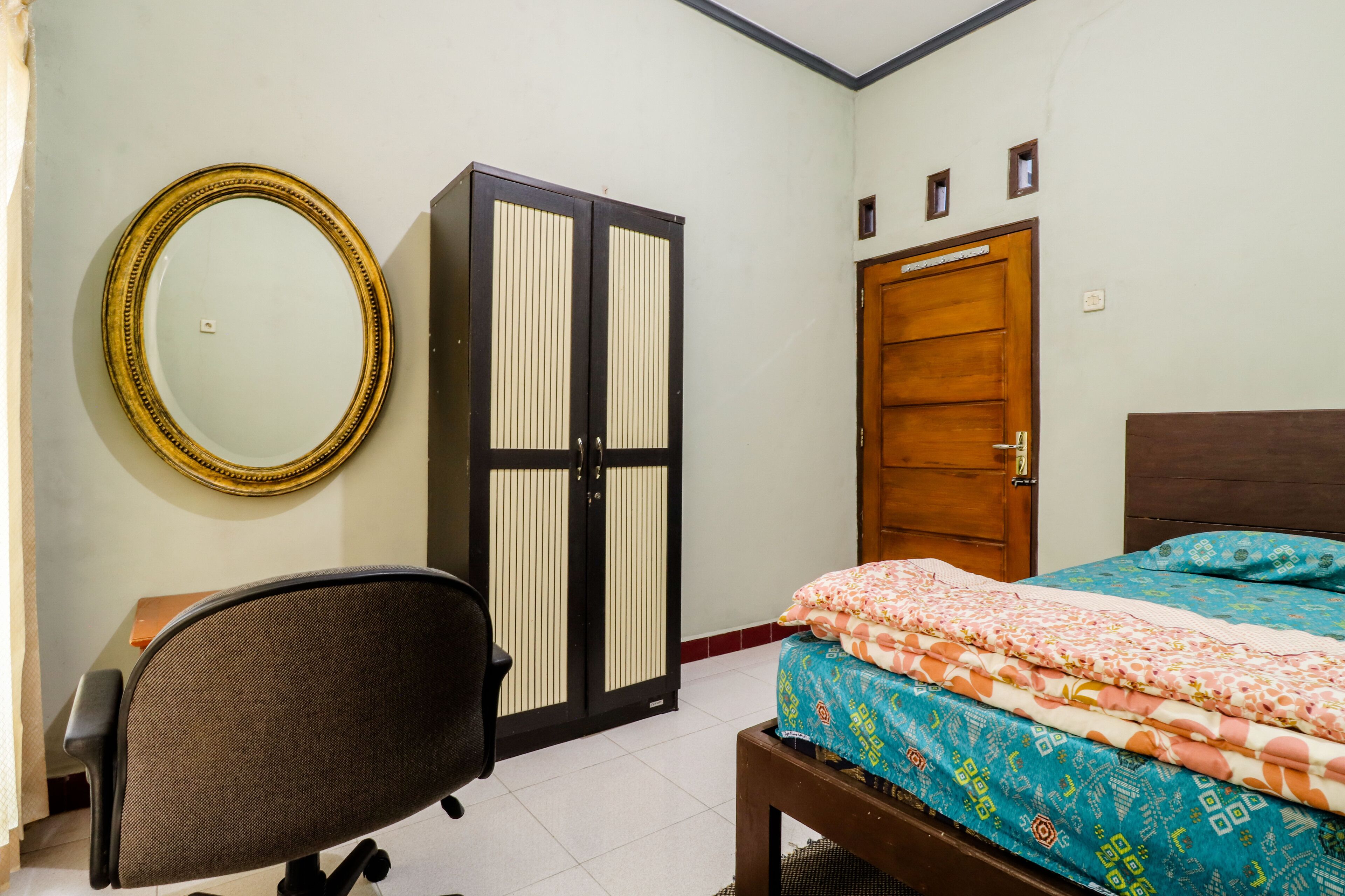 A bedroom with a bed, a desk, a chair, a wardrobe, and a mirror.
