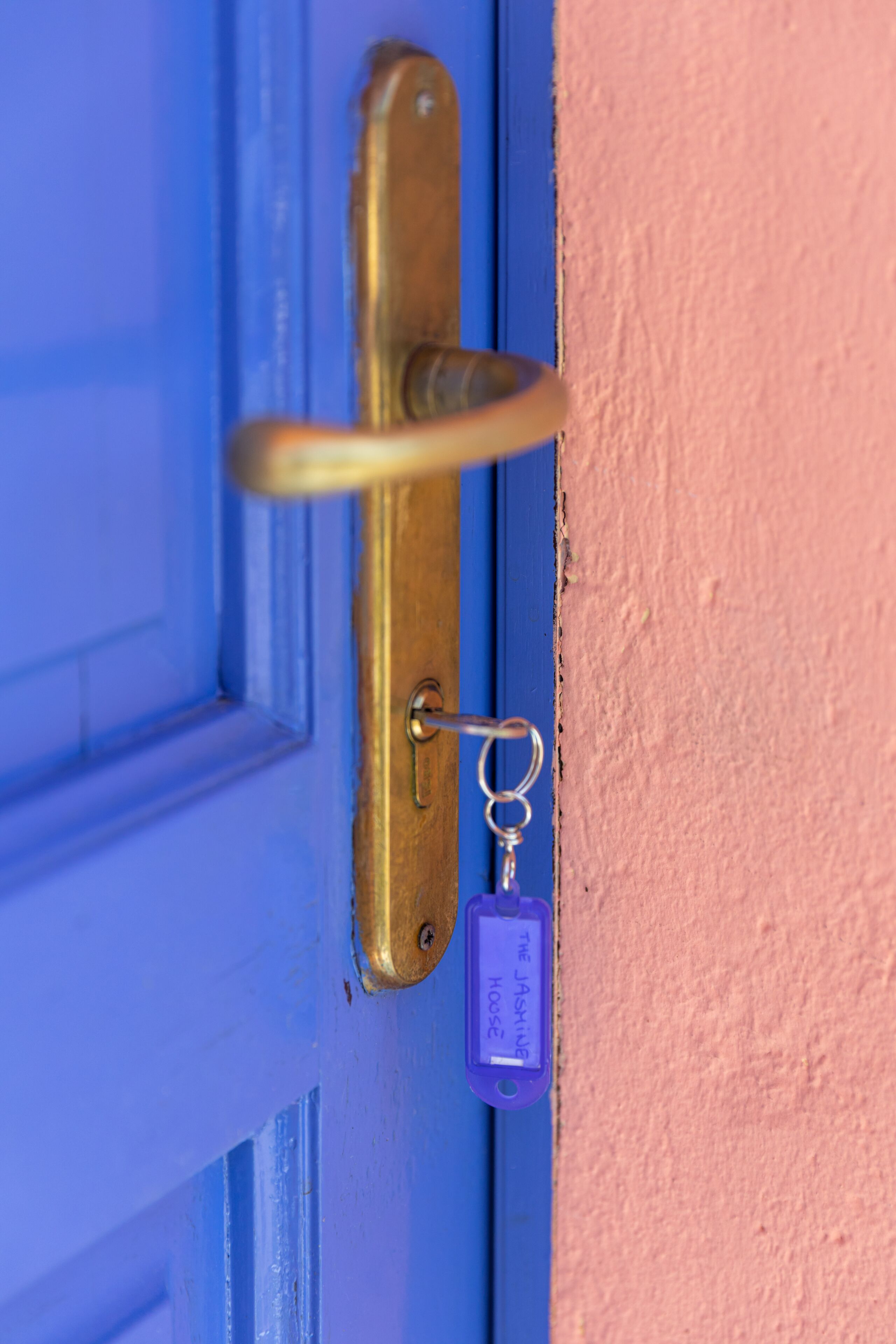 A blue door with a brass handle and a keychain labeled "The Jasmine House."