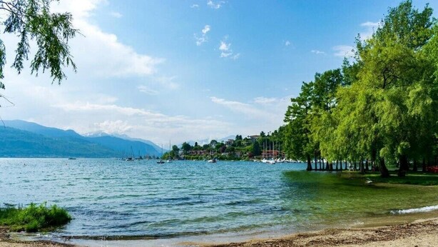 A lakeside view with a sandy beach, trees, and boats in the distance. - A Country House near the Lake Cod. 012104-CNI-00006 IT012104C24MJ5EPRC (Monvalle)