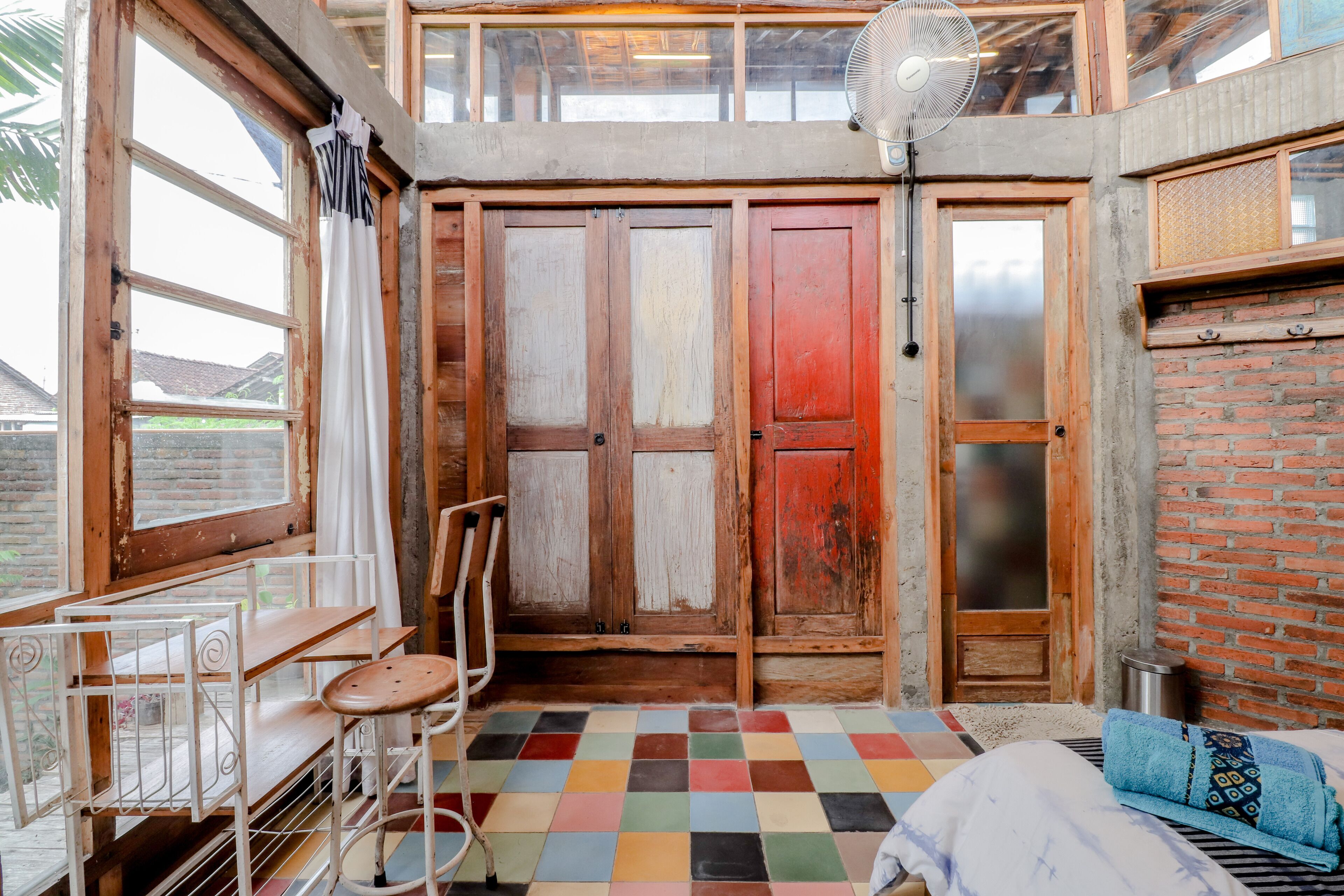 A room with a checkered floor, a bed, a fan, and a window with curtains.