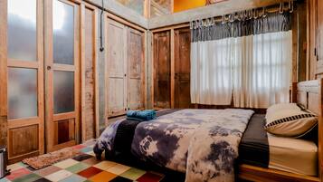 Une chambre avec un lit en bois, un sol à carreaux aux couleurs vives et une grande fenêtre avec des rideaux.