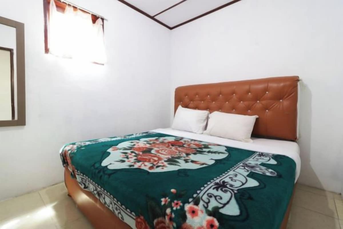 Un dormitorio con un cabecero tapizado en marrón, una colcha con estampado floral y almohadas blancas.