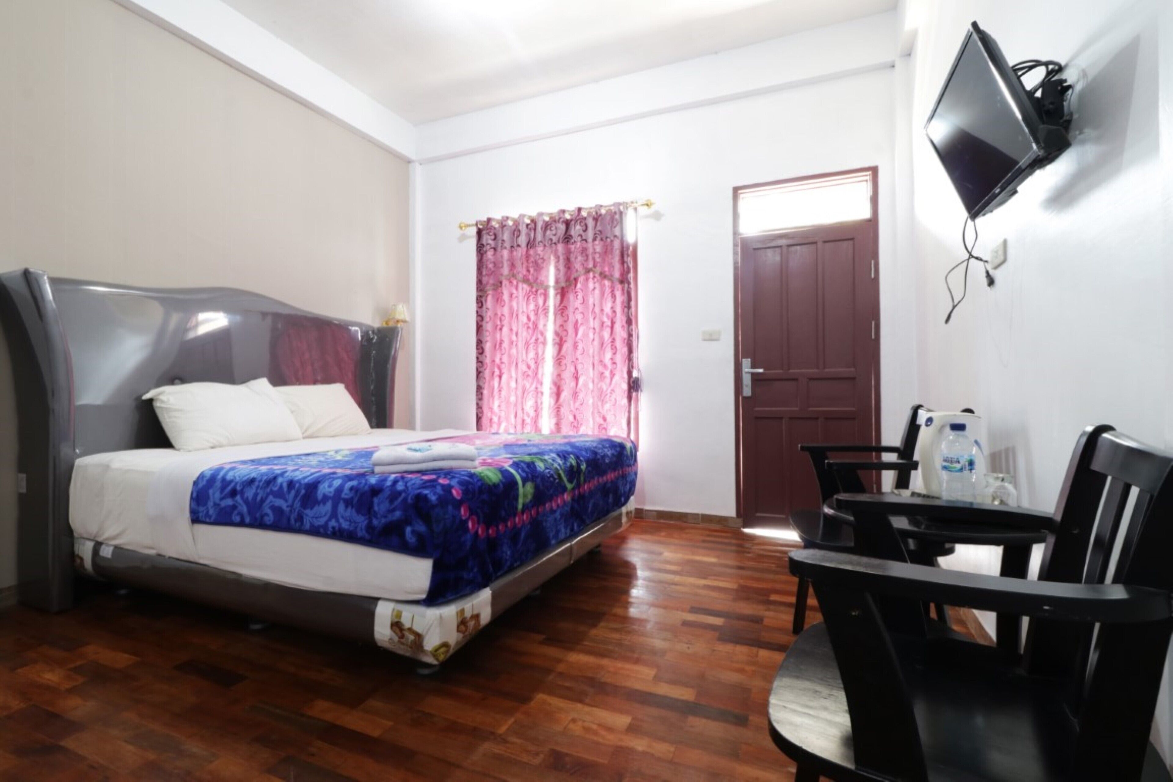 Un dormitorio con cama, escritorio, silla, televisor y puerta.