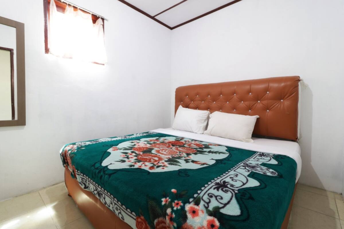Een slaapkamer met een bruin gestoffeerd hoofdeinde, een bloemenprint beddegoed en witte kussens.