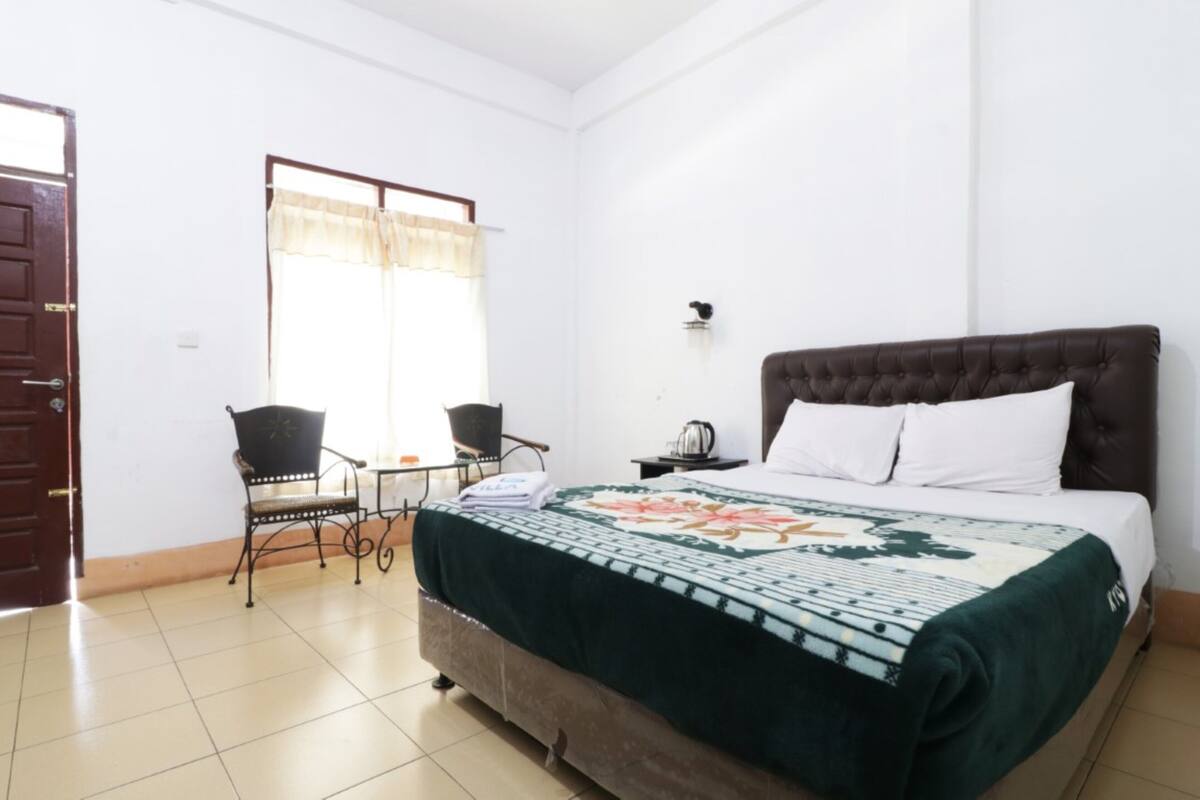 Een slaapkamer met een bed, een stoel, een tafel en een raam met gordijnen.