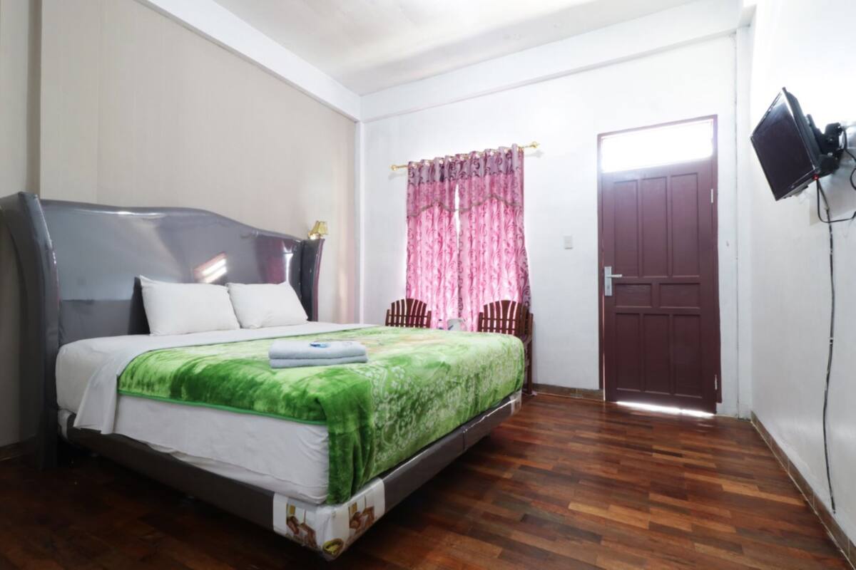 Een kamer met een bed, een houten vloer, een deur en een aan de muur bevestigde televisie.