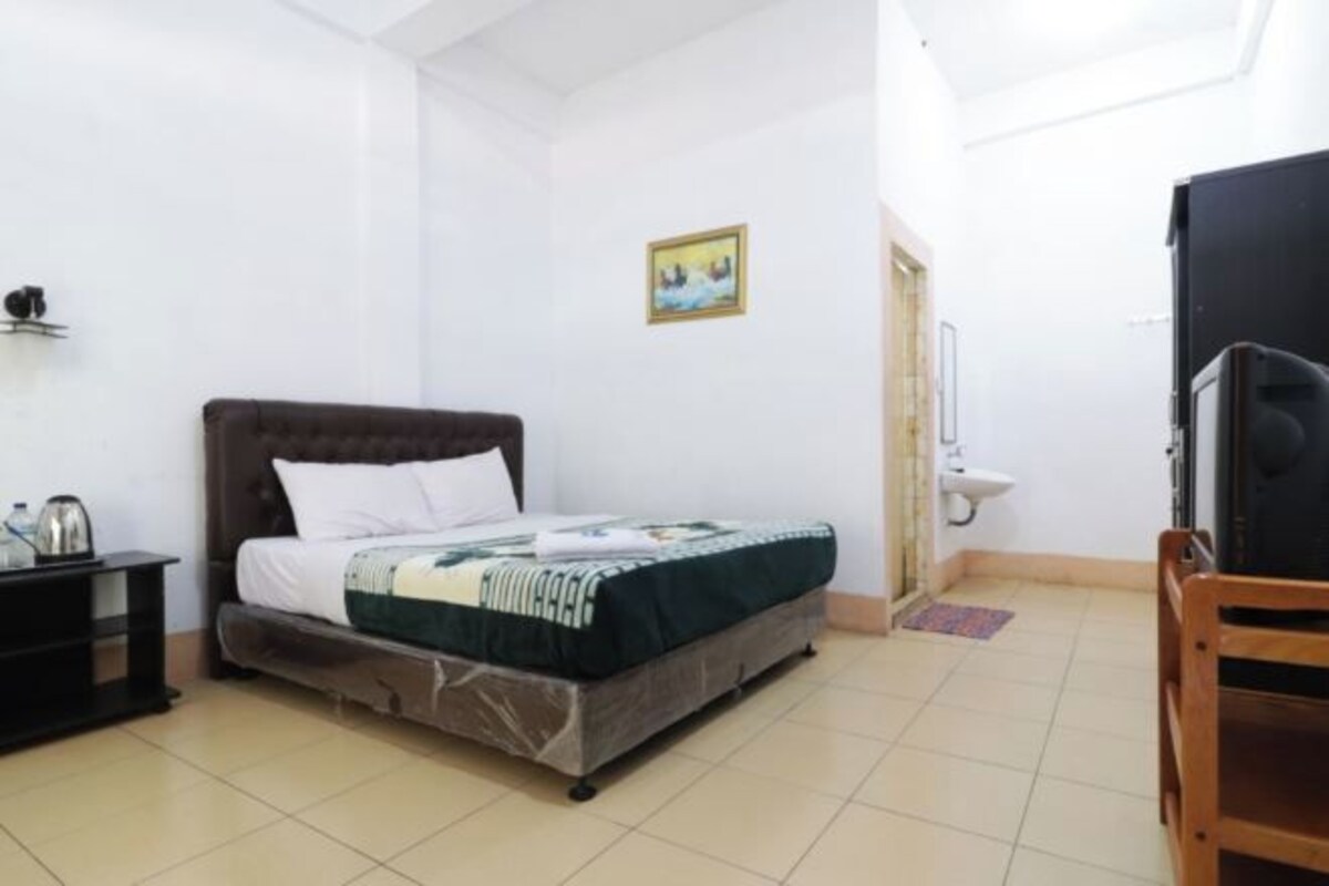 A bedroom with a bed, a nightstand, a chair, a sink, and a door.