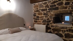 Une chambre avec un mur en pierre, un lit avec une literie blanche, une table de chevet et une bougie allumée.
