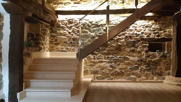 Un escalier en pierre menant à un niveau supérieur, avec une main courante en bois et une balustrade en verre.