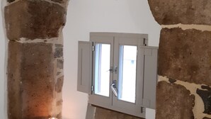 Un mur de pierre avec une fenêtre et une bougie posée sur une étagère.