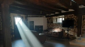 Un intérieur rustique avec un mur en pierre, une cheminée, un canapé et un téléviseur fixé au mur.